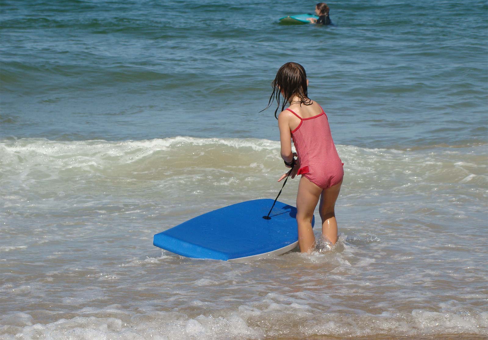 A little girl at the water's edge with a bodyboard