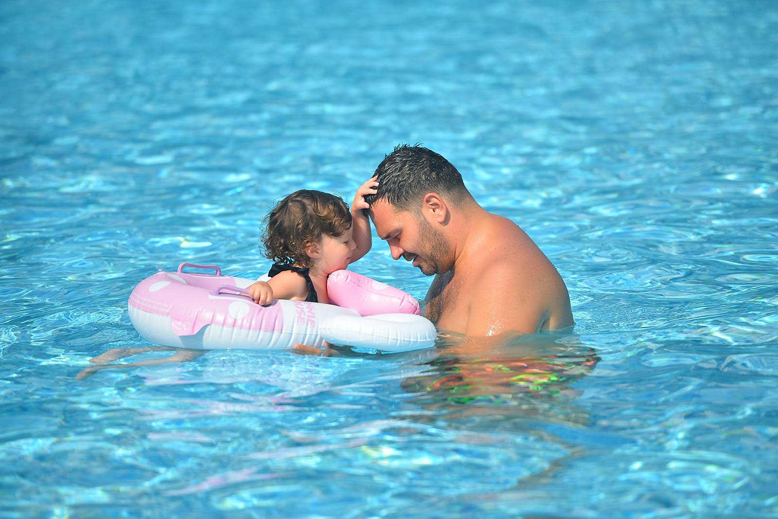 Little girl in her buoy with her father in the swimming pool at the campsite in Oléron