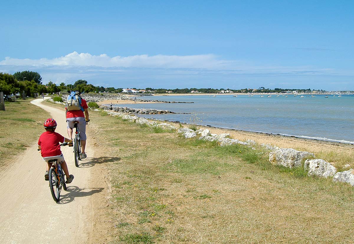 Enfant et son père à vélo sur une piste cyclable devant une plage à Oléron