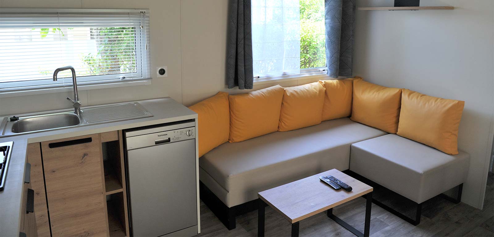 Kitchen area and gray and yellow sofa in a mobile home for rent in Oléron
